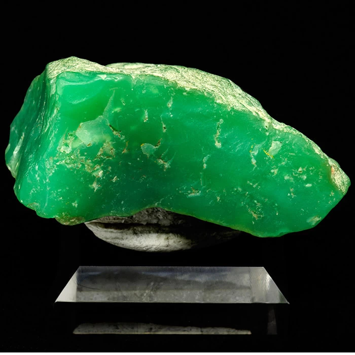 emerald green coloured chrysoprase mineral. A rough piece on a small stand.