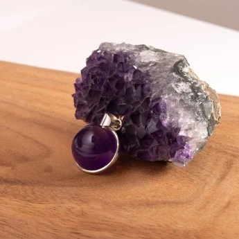 round sterling silver pendant featuring a bulbous amethyst cabochon. The pendant is in front of an amethyst geode